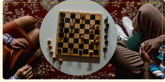 Twee mensen spelen schaak aan een ronde witte tafel, met op de achtergrond een tapijt met patronen.